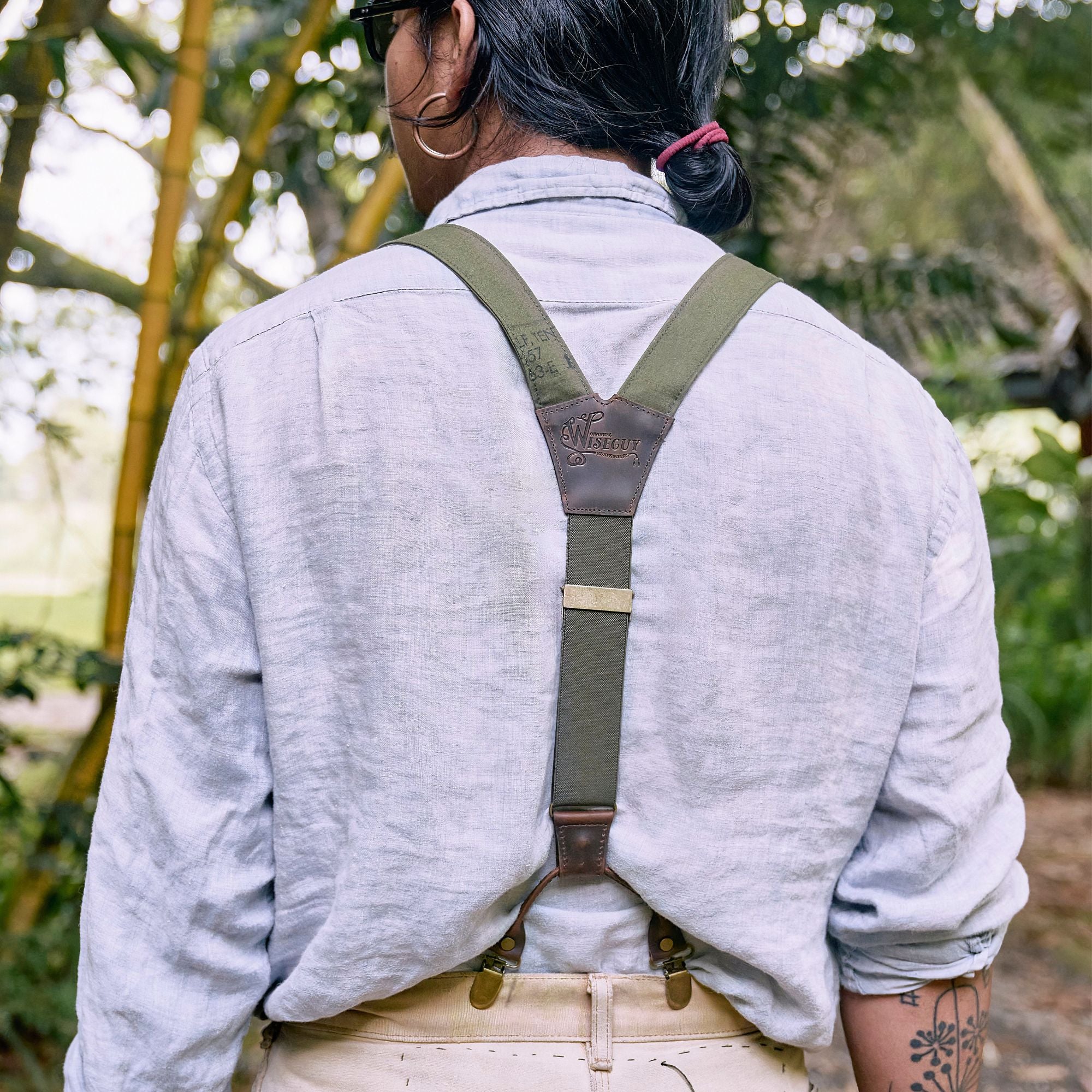 Back of man wearing a light blue linen shirt and army green Wiseguy Original Suspenders.