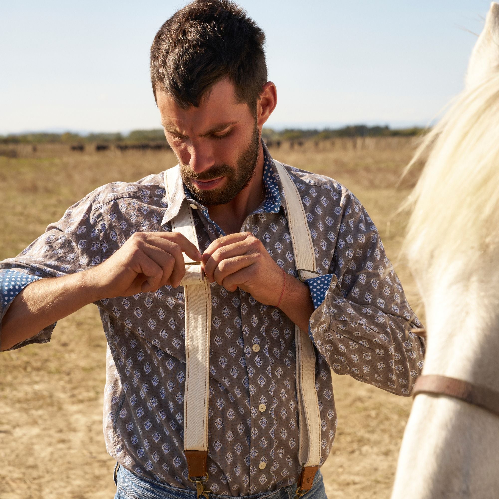 Man wearing white canvas suspenders and a pattered shirt. 