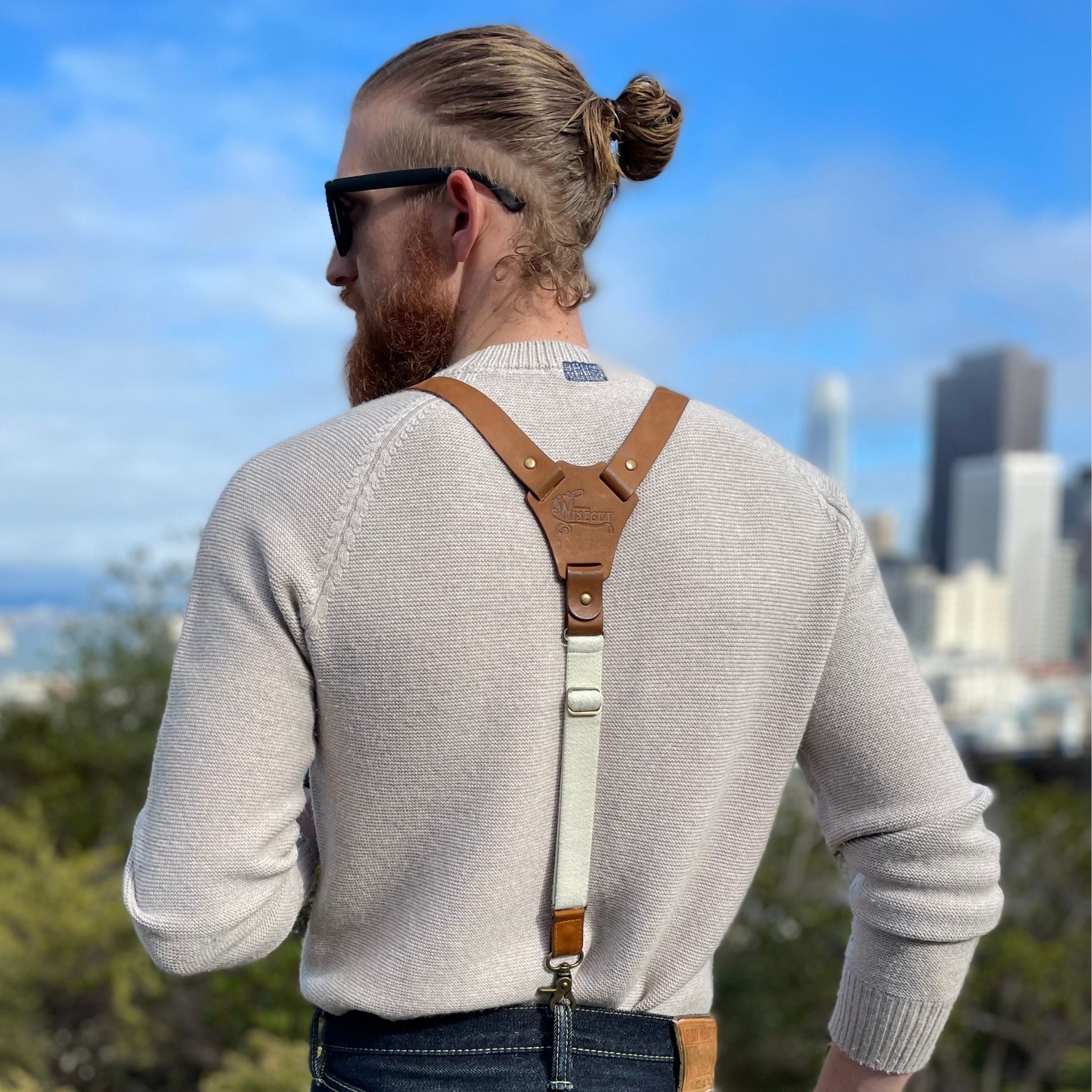 Man photo from the back with skyline in the background. He is wearing Suspenders and has his hair in a bun.